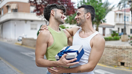 Two men couple smiling confident surprise with birthday gift at street