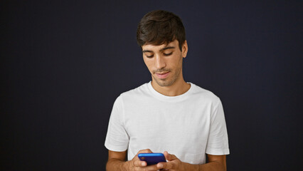 Cool young hispanic man engrossed in avidly texting a serious message online. he uses smartphone...