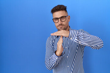 Hispanic man with beard wearing glasses doing time out gesture with hands, frustrated and serious...