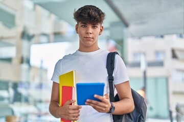 Naklejka premium Young hispanic teenager student using touchpad holding books at university