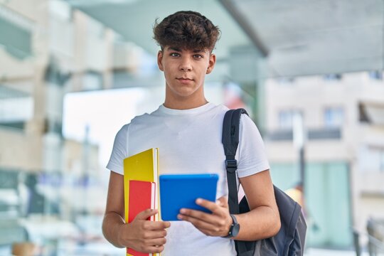 Young hispanic teenager student using touchpad holding books at university