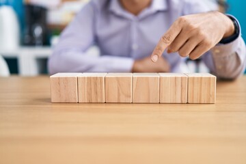 Young hispanic man business worker sitting on table with wooden cubes at office