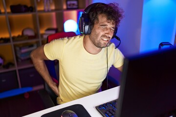 Young hispanic man streamer using computer suffering for backache at gaming room