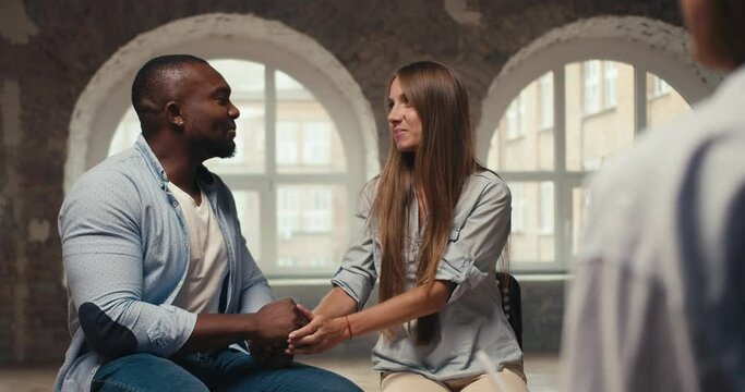 Happy couple, a fit man with black skin in a blue shirt and a blonde girl are talking with a psychologist. Personal conversation and therapy with a psychologist in a brick building