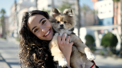 Obraz premium Young hispanic woman with dog smiling confident standing at street