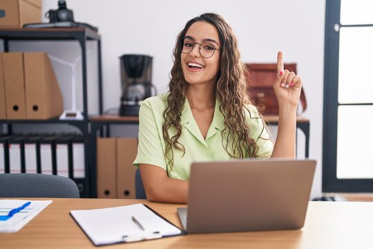 Young hispanic woman working at the office wearing glasses pointing finger up with successful idea. exited and happy. number one.