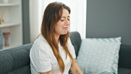 Young beautiful hispanic woman sitting on the sofa crying at home