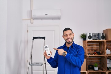 Hispanic repairman working with air conditioner smiling happy pointing with hand and finger