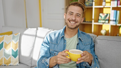 Young caucasian man drinking coffee sitting on sofa at home