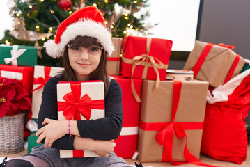 Obraz na płótnie Canvas Adorable hispanic girl hugging christmas gift sitting on floor at home