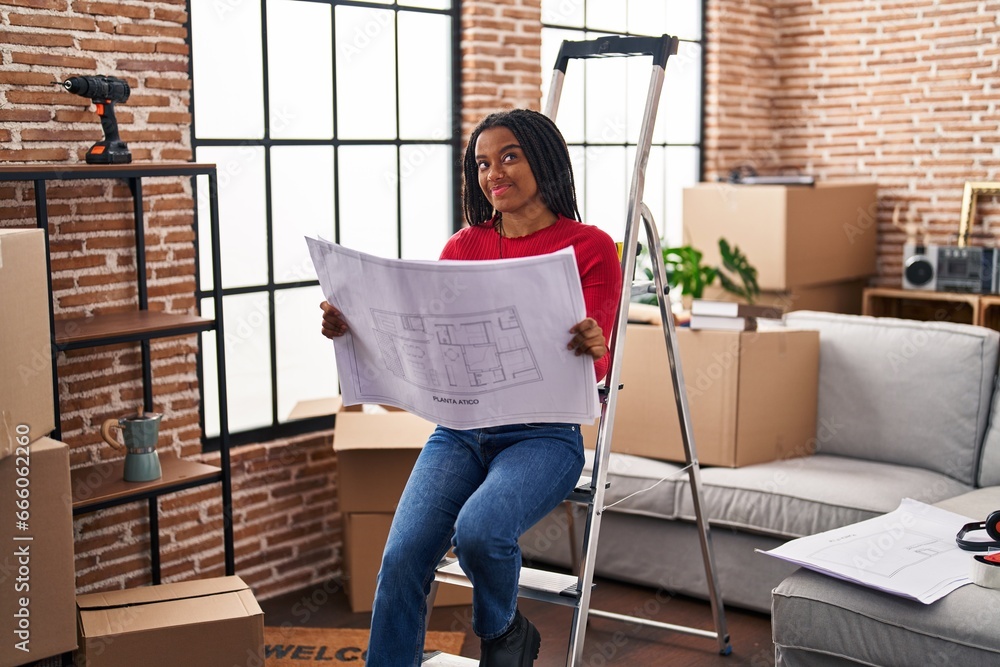 Poster Young african american with braids standing on new home looking at blueprints smiling looking to the side and staring away thinking.