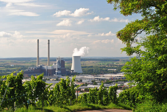 View of Cooling Tower and Industrial Chimneys from Tree Covered Hill on Sunny Day