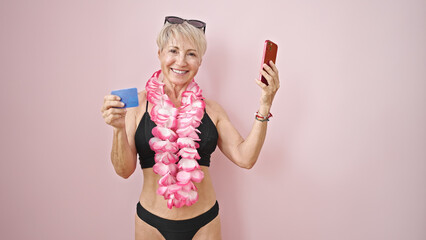 Middle age blonde woman wearing bikini and hawaiian lei shopping with smartphone and credit card...