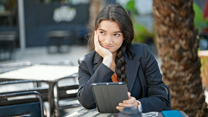 Young beautiful hispanic woman business worker using touchpad sitting on table at coffee shop terrace