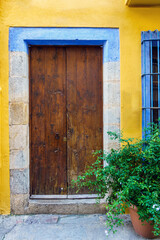 Fototapeta na wymiar Colorful facade with an old wooden door, plants on the ground in a mediterranean village