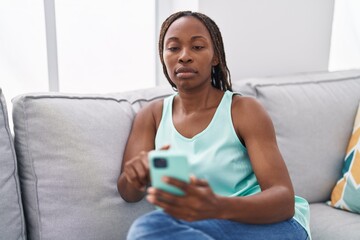African american woman using smartphone with serious expression at home