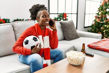 African american woman supporting soccer team talking on smartphone at home