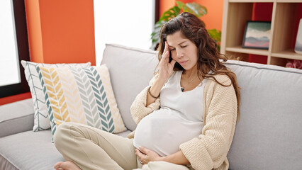 Young pregnant woman suffering for headache sitting on sofa at home