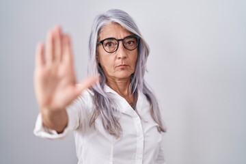 Middle age woman with tattoos wearing glasses standing over white background doing stop sing with palm of the hand. warning expression with negative and serious gesture on the face.