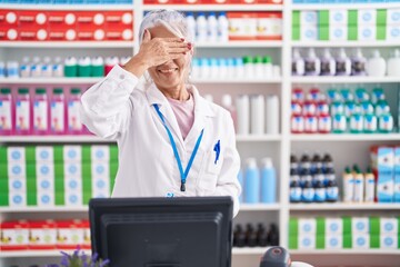 Middle age woman with tattoos working at pharmacy drugstore smiling and laughing with hand on face covering eyes for surprise. blind concept.