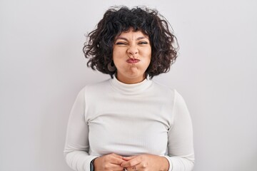 Hispanic woman with curly hair standing over isolated background puffing cheeks with funny face. mouth inflated with air, crazy expression. - obrazy, fototapety, plakaty