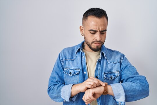 Young hispanic man standing over isolated background checking the time on wrist watch, relaxed and confident