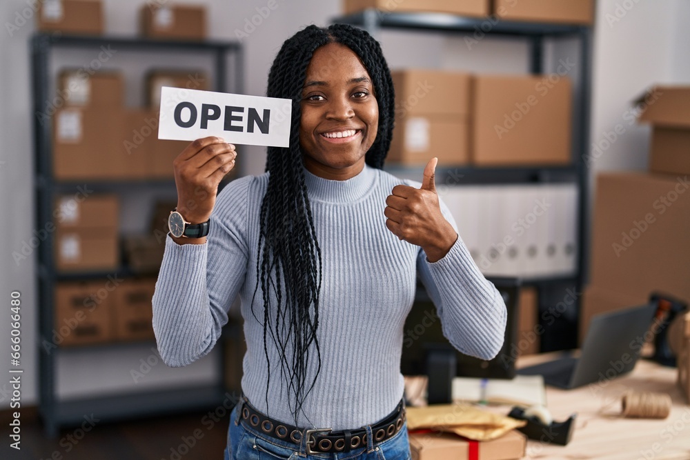 Sticker African american woman working at small business ecommerce holding open banner smiling happy and positive, thumb up doing excellent and approval sign