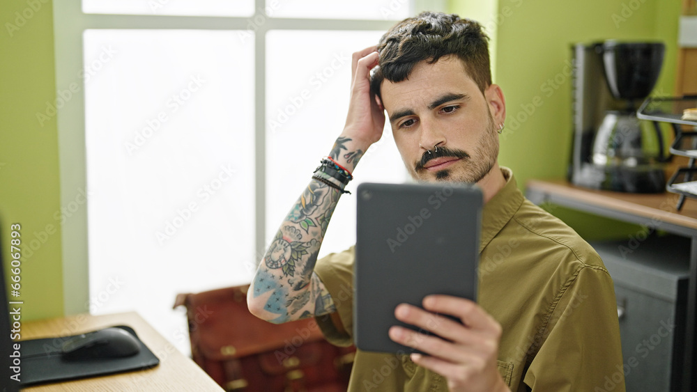 Poster Young hispanic man business worker combing hair looking on touchpad at office