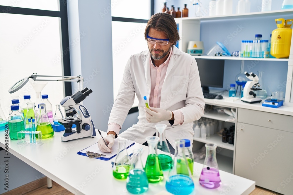 Sticker Middle age man scientist holding test tube writing on document at laboratory