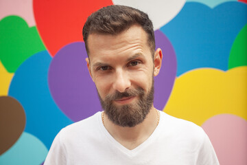 Fototapeta premium Love concept. Portrait of proud charismatic active 30-year-old man posing over colourful background. Perfect haircut. Hipster style. Close up. Outdoor shot