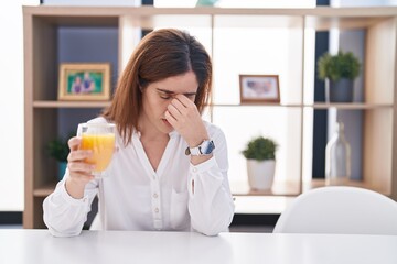Brunette woman drinking glass of orange juice tired rubbing nose and eyes feeling fatigue and...