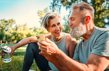 Active seniors on fresh air. Cheerful husband and wife sitting on grass after morning exercises in...