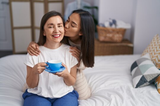 Two women mother and daughter hugging each other drinking coffee at bedroom
