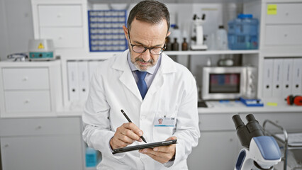 Middle age man with grey hair, a dedicated scientist, engrossed in his research on a touchpad at...