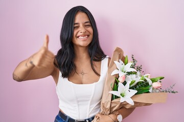 Brunette woman holding bouquet of white flowers approving doing positive gesture with hand, thumbs up smiling and happy for success. winner gesture.