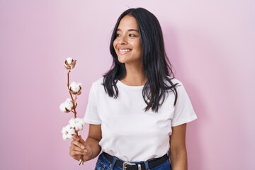 Brunette woman standing over pink background looking away to side with smile on face, natural expression. laughing confident.