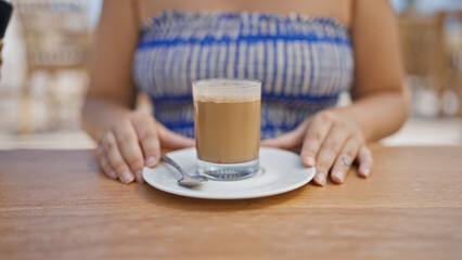 Young hispanic woman stirring coffee sitting on the table at sunny restaurant terrace