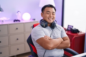 Young chinese man streamer smiling confident sitting with arms crossed gesture at gaming room
