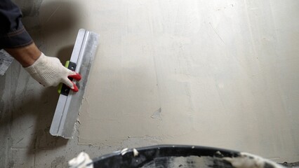 The master applies putty to the white wall to level it. A plasterer smoothest wet plaster on a wall...