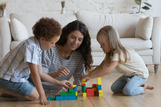 Happy pretty 30s mom and two focused engaged preschool little kids playing on heating floor together, building towers, toy castle from colorful blocks, enjoying family creative game, home activity