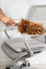 The man cleans the chair with a chicken feather duster.