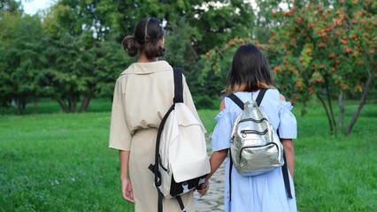 Two girls walking in the park in the summer, talking, walking after school and college, holding hands, best friends, sisters returning home after school