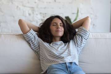 Calm lazy beautiful adult Hispanic woman relaxing on comfortable couch at home, taking nap, meditating, breathing fresh air, enjoying leisure, break, weekend, stress relief