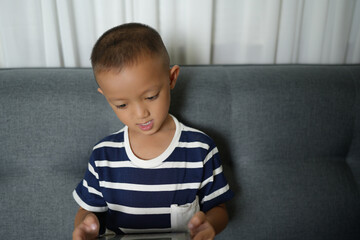 Asian boy uses tablet to watch video clips on sofa in home