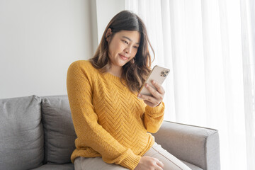 Pregnant asian woman holding smartphone at home using mobile app for pregnant women