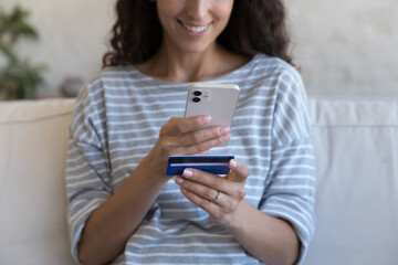 Fototapeta premium Happy smartphone user woman holding credit card, inserting data for buying on internet store website, online payment, using banking ecommerce app. Close up of hands, cropped shot