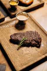 Fresh juicy delicious beef steak on wooden background in restaurant. Meat dish with spices and herbs