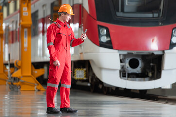 Portrait of a technician using a mobile phone in front of a train while relaxing after inspecting the electric train's machinery repairs.