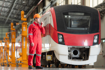 Portrait of a technician using a walkie talkie in front of a train for communicate with his co-workers after inspecting the electric train's machinery repairs.