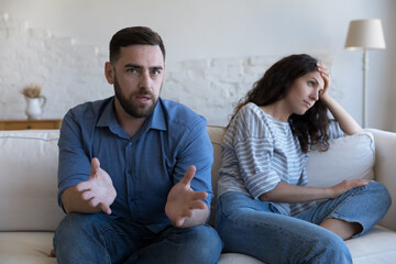 Tired married couple taking online counseling, husband speaking at camera, annoyed wife touching head, looking away, sitting on sofa at home, going through relationship crisis, problems